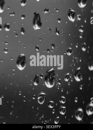 Close view of water droplets on window glass, with sharp highlights and soft blur in black and white, forming moody abstract texture for weather, back Stock Photo