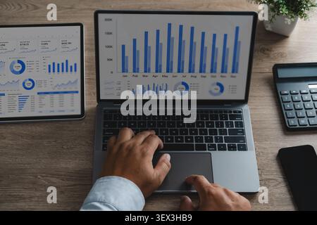 Hands analyzing financial data on laptop and tablet screens with charts, dashboard, and calculator on wooden desk for business reporting, performance Stock Photo