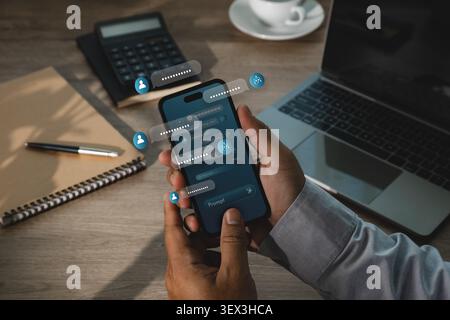 Hand uses smartphone with AI chatbot interface, floating message bubbles, prompt icons and laptop workspace, showing digital assistant communication a Stock Photo