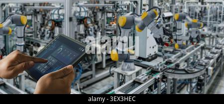 Hands use a tablet dashboard to control and monitor robotic machines on an automated factory line, showing industrial automation, production supervisi Stock Photo