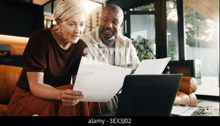 Interracial couple, laptop and reading with documents in home for finance, bills or investment. Mature man, woman and paperwork with tech for Stock Photo