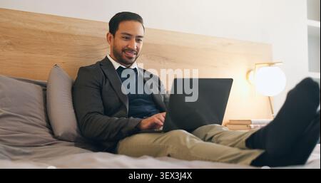 Happy, man and relax in bedroom with laptop, social media and browsing website to unwind. Smile, male person and rest on bed at house with tech Stock Photo