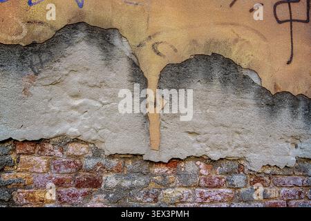 Plaster falling off of an old brick wall. Old cracked and ruined wall made of red bricks with remains of plaster in Venice, Italy Stock Photo