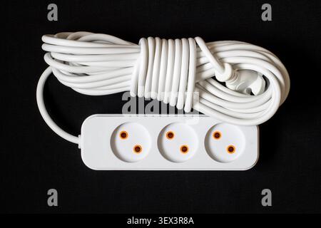 White electric extension cord on a dark background. Long electrical wire with sockets. Stock Photo