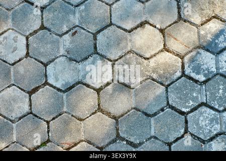 Full frame background of old weathered grey hexagonal concrete paving tiles with natural shadows and sunlight. Textured geometric stone pavement block Stock Photo