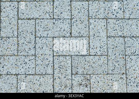 Full frame background of weathered grey terrazzo paving bricks laid in a herringbone pattern. Textured speckled stone pavement blocks background for a Stock Photo