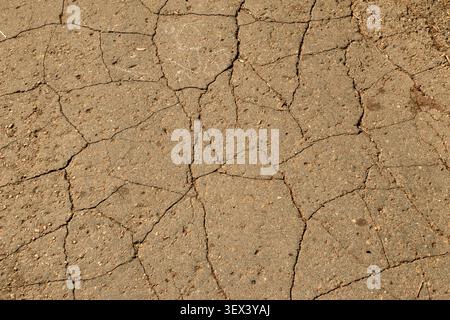 Full frame background of old cracked asphalt pavement surface in daylight. Textured brown damaged road with deep fissures and lines pattern for constr Stock Photo