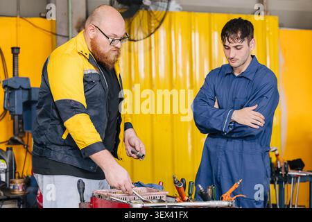Mechanic worker in garage auto service center working service maintenance modern car with professional skill and safety uniform. Stock Photo