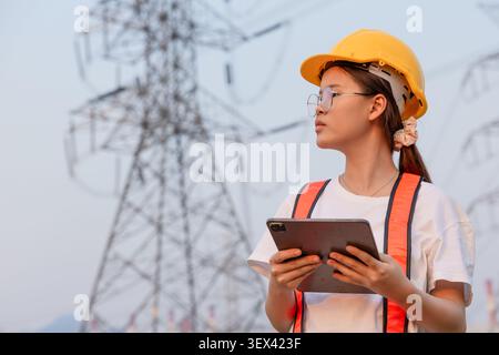 Female engineer inspecting power transmission tower, energy infrastructure concept, electricity industry, utility maintenance, engineering inspection, Stock Photo