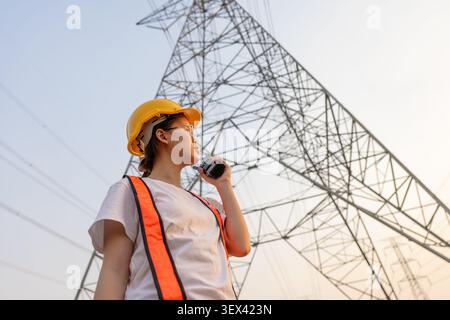 Female engineer inspecting power transmission tower, energy infrastructure concept, electricity industry, utility maintenance, engineering inspection, Stock Photo