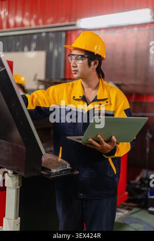 Asian Engineer male worker work control operate machine control panel in metal part workshop plant factory with safety uniform. Stock Photo