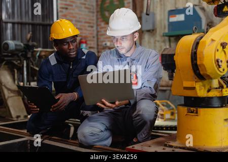 Professional engineer workers team working in metal workshop talking and working together fixing service maintenance robot machine. Stock Photo