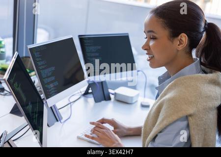 Female developer coding on multiple monitors in office Stock Photo