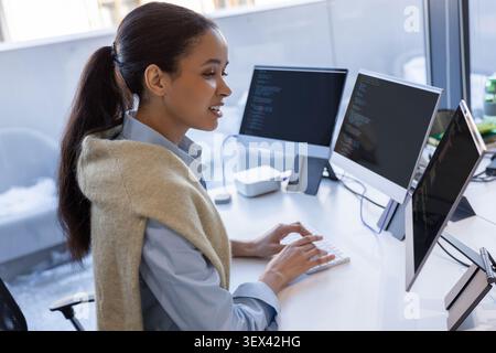 Young woman writing code on several screens in office Stock Photo