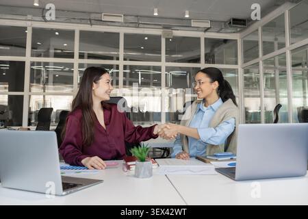 Two successful businesswomen handshaking at conference desk Stock Photo
