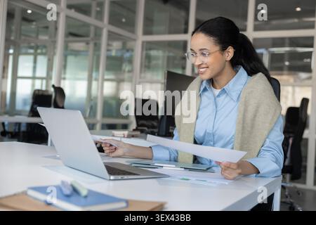 Businesswoman in glasses working on laptop with documents Stock Photo