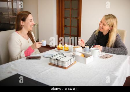Two smiling women sharing a relaxing breakfast and conversation at home Stock Photo