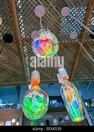 Three multi colored decorative lamps dangle from a ceiling made of wood. They create bright patterns in a shop that focuses on home decor and lighting Stock Photo