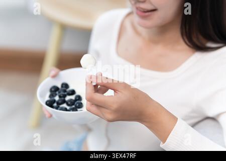 Asian Woman having delicious healthy breakfast at home on morning. Health care female eats yogurt with granola and berry fruit. Healthy food, Vitamins Stock Photo