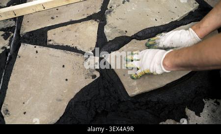 Construction worker carefully placing irregular shaped stone on wet mortar during a paving project Stock Photo
