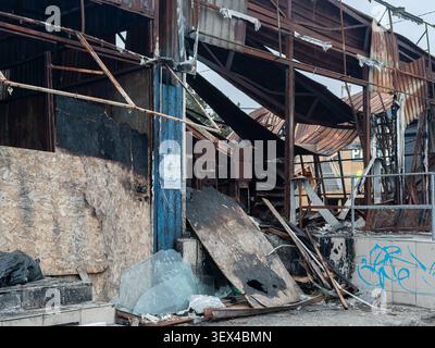 The scorched remnants of a commercial facility showcase destroyed steel beams and broken plywood, illustrating severe fire damage, structural decay, a Stock Photo