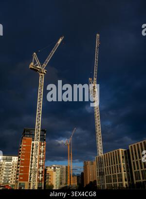 Construction cranes towering above city skyline against dramatic dark stormy sky Stock Photo