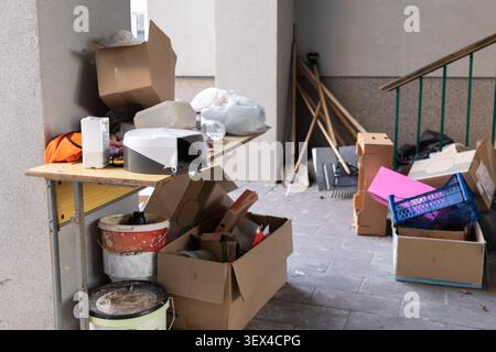 Stacked piles of empty carton boxes, trash, and old tools gathered in a dim corridor area, representing themes of cleaning, home maintenance, moving h Stock Photo