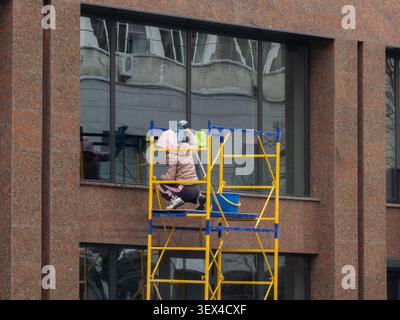 This person cleans large windows on scaffolding outside an office building to emphasize professional exterior maintenance and property care within a b Stock Photo