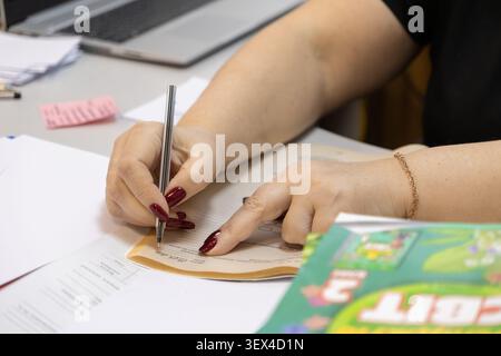 A student or teacher writes notes in a workbook at a desk with papers and a laptop to capture the essence of diligent study, task management, and prof Stock Photo