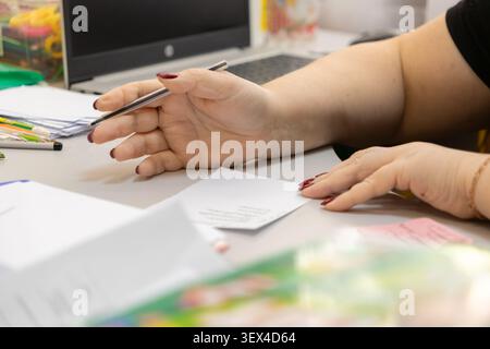 Professional hand grips a pen while working on documents, representing focused productivity and administrative tasks within an efficient, well-lit ind Stock Photo