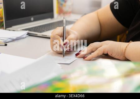 Close-up of a person hands jotting down quick notes on a paper slip at a workstation with a laptop, reflecting concentrated organizational habits and Stock Photo