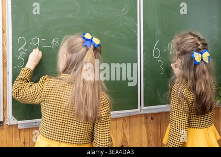 Schoolgirls wearing matching outfits solving math problems on a chalkboard, illustrating a collaborative educational experience in a classroom that fo Stock Photo