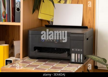 This compact color printer with refillable ink reservoirs stands on a desk shelf to represent organized document management and productive technology Stock Photo