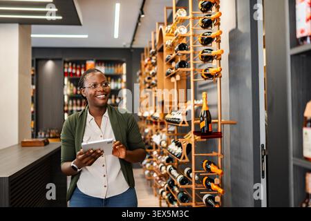 Woman sommelier checking inventory in wine shop holding digital tablet and smiling Stock Photo