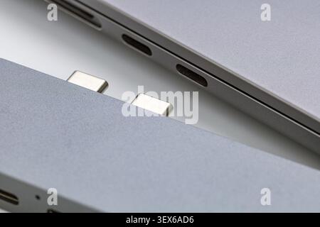 Macro close up of two modern silver aluminum portable computing devices showing USB Type C ports and metallic magnetic connector pins, highlighting sl Stock Photo