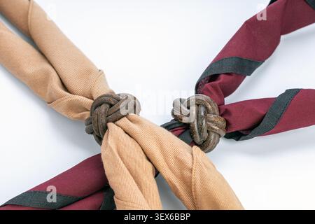 Traditional Thai scout neckerchiefs in beige and maroon colors secured with handcrafted leather Turk's head woggle knots, displayed on a clean white b Stock Photo