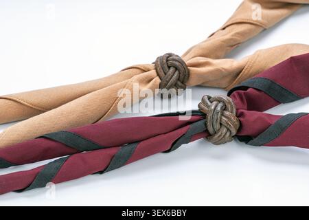 Close up of two traditional Thai scout neckerchiefs, khaki and maroon with black stripe, fastened by handmade braided leather Turk's head woggle knots Stock Photo