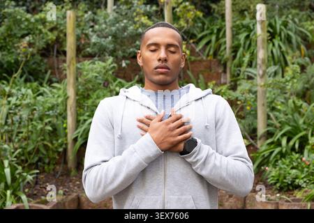 African American man standing hands crossed at chest in yard wearing gray hoodie, black smartwatch Stock Photo