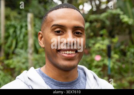 African American man in his 20s smiling and wearing gray hoodie, hoop earring, garden background Stock Photo