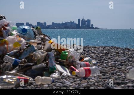 Plastic waste and trash piled up on the pebble beach, with the city in the background, highlighting pollution and the impact of human activities near Stock Photo