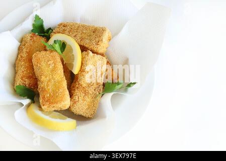 Homemade breaded fish sticks served with fresh lemon slices and parsley garnish, white background, closeup, top view. Stock Photo