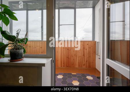 view from inside a room, looking out onto a balcony with wooden walls and large windows showing a cloudy sky Stock Photo