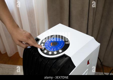A detailed close-up shot of a woman's hand touching the modern circular blue LED touchscreen display panel on top of a black and white climate control Stock Photo