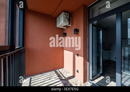 modern balcony with terracotta walls, sleek black window and door frames, and stylish herringbone flooring. Features air conditioning and minimalist s Stock Photo