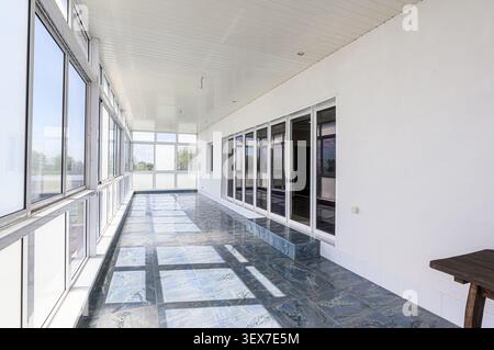 Bright, enclosed patio with glass windows on one side and sliding doors on the other. Blue marble-style tile flooring adds contrast to the white walls Stock Photo