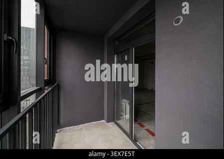Balcony with gray walls, black railing, and glass door to an empty room. Neutral tones and modern architectural details Stock Photo