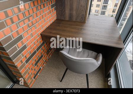 cozy workspace featuring a wooden desk, brick wall, and stylish gray chair. Natural light streams in, highlighting the textures and creating a modern, Stock Photo
