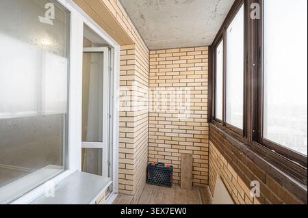 view of a balcony with light brick walls, brown-framed windows, and a white-framed door. Stock Photo