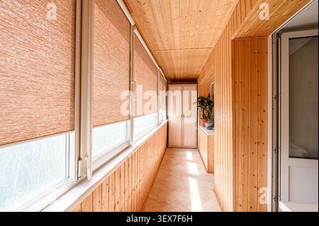 cozy balcony with wood paneling, blinds on windows, and warm lighting. The space is well-lit with sunlight streaming through the window Stock Photo
