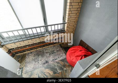 High-angle shot of an interior space featuring a red beanbag, brick wall, rug, and skylights, creating a cozy and modern look Stock Photo